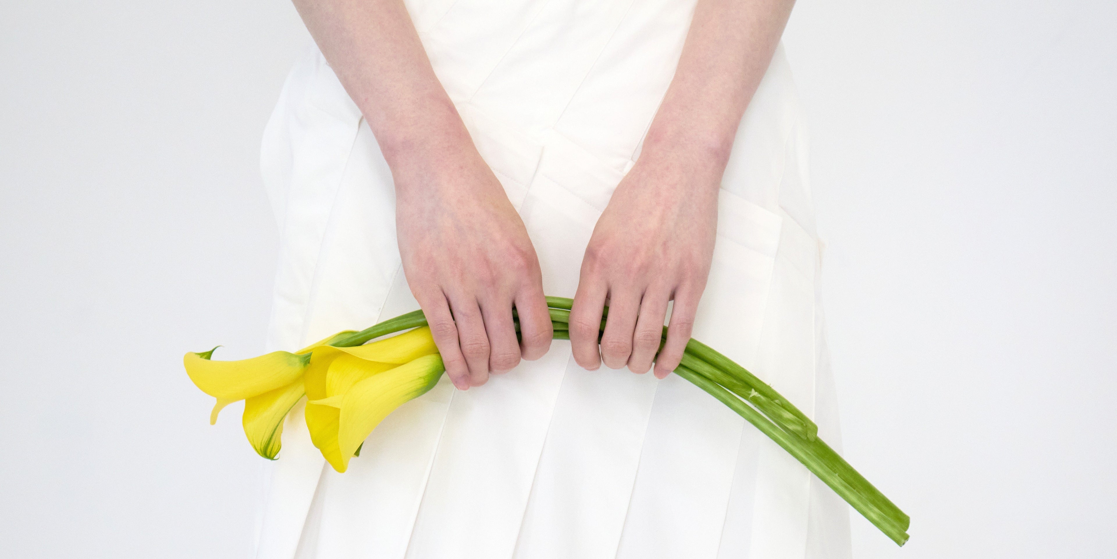 Person holding yellow flowers against white fabric showcasing the difference between low and high quality fabric