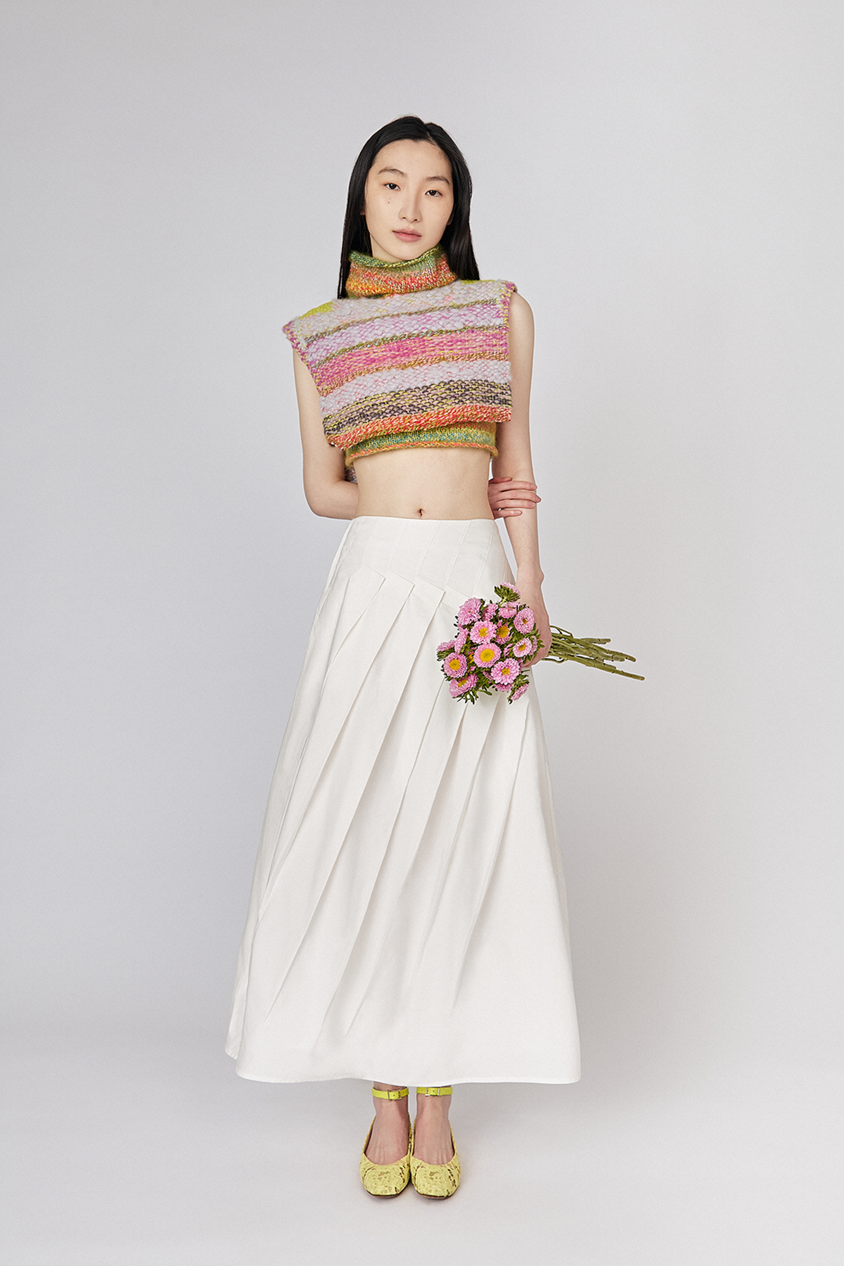 Full length view on model wearing Du & Berry Du White Cotton Poplin Pleated Midi Skirt and Du & Berry One of A Kind knit cropped Wool Cashmere Turtleneck Top holding flowers