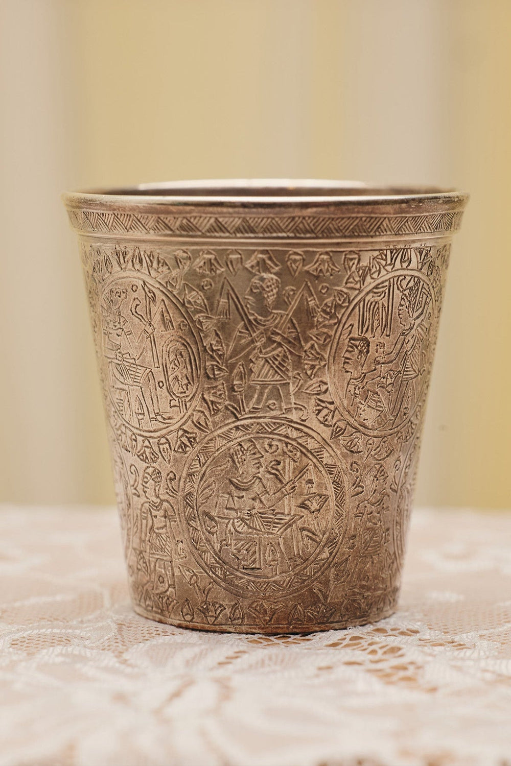 Model's hand holding the Egyptian Revival Sterling Silver Cup from Du & Berry's curated vintage collection. Image shows close-up view of Egyptian etchings all over cup.