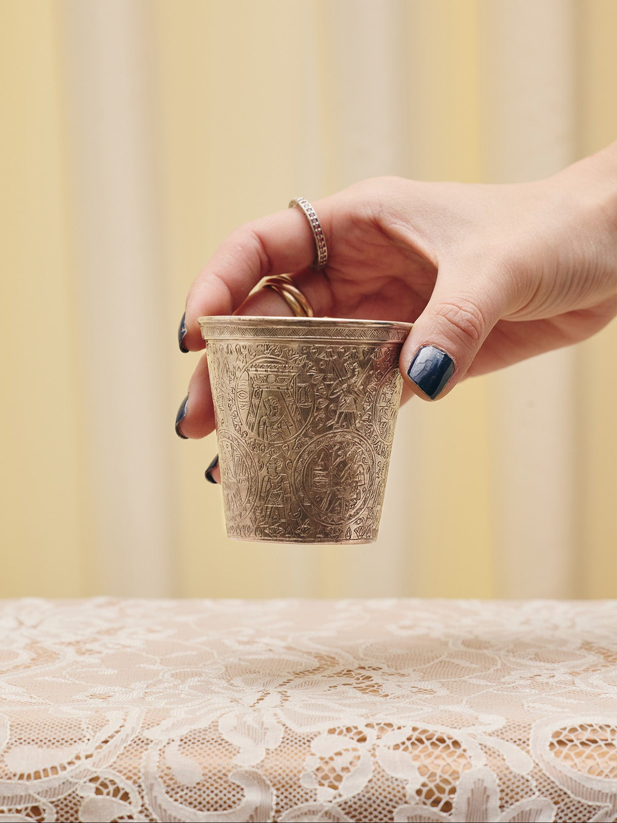 Model's hand holding the Egyptian Revival Sterling Silver Cup from Du & Berry's curated vintage collection. Image shows close-up view of Egyptian etchings all over cup.