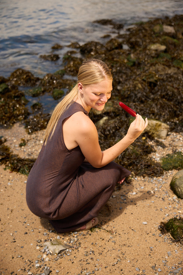 Woman wearing Du & Berry brown linen side split maxi dress sitting on sandy shore near water