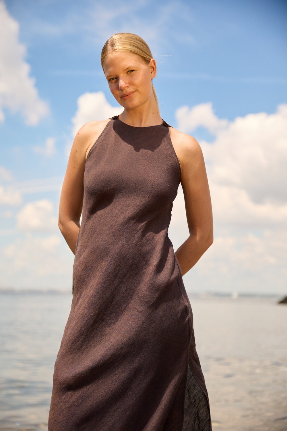 Du & Berry Brown Linen Side Split Maxi dress worn by woman standing near water under blue sky