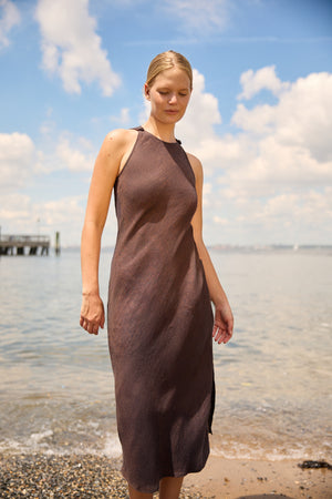 Brown Linen Side Split Maxi dress by Du & Berry worn by woman standing on a beach under blue sky