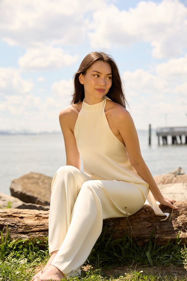 Woman wearing Du & Berry Cream Comfort Straight Pants sitting on a log by the water on a sunny day
