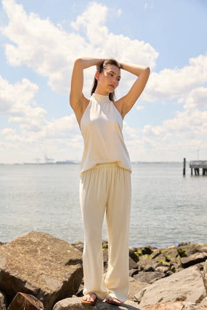 Woman wearing Du & Berry Cream Comfort Straight Pants standing on rocks by the water on a sunny day