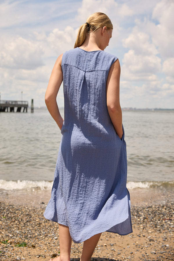 Woman wearing Du & Berry Blue Linen Button Midi Dress standing on a pebbled beach with ocean background