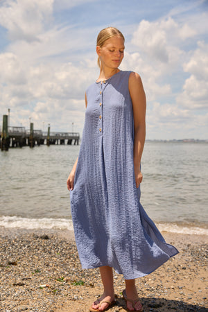Du & Berry Blue Linen Button Midi Dress sleeveless flowy dress worn by a woman on the beach