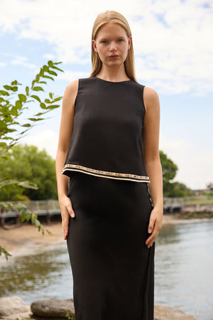 Du & Berry black linen top skirt set worn by model standing near water with natural background