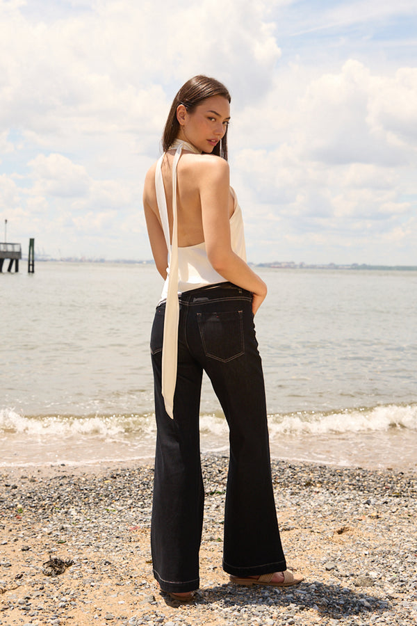 Woman wearing Du & Berry navy flare jeans for women standing on a beach with a white halter top