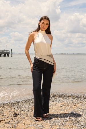 Woman wearing navy flare jeans for women by Du & Berry standing on a beach with a cream halter top