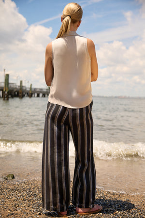 Woman wearing Du & Berry Navy Linen Wide Leg Stripe Pants standing on a beach with water and sky background