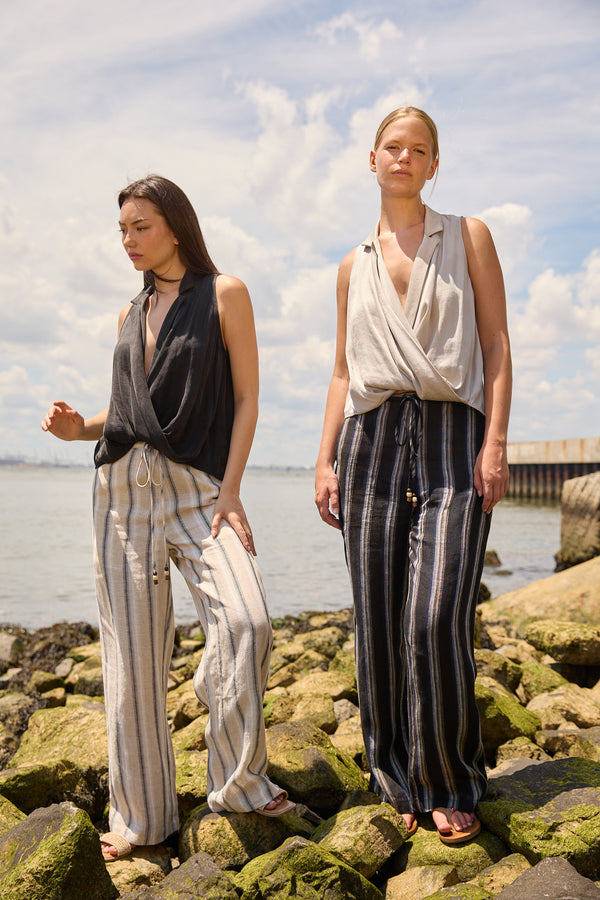Two models wearing Du & Berry Navy Linen Wide Leg Stripe Pants standing on rocky shore under cloudy sky