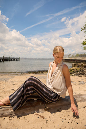 Woman wearing Du & Berry Navy Linen Wide Leg Stripe Pants sitting on a log at the beach under a blue sky