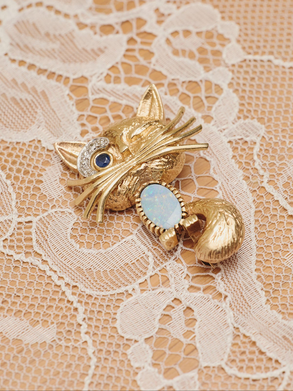 Du & Berry curated vintage - 14K gold winking cat brooch/lapel pin with opal belly, diamond brow, and sapphire eye lying on table