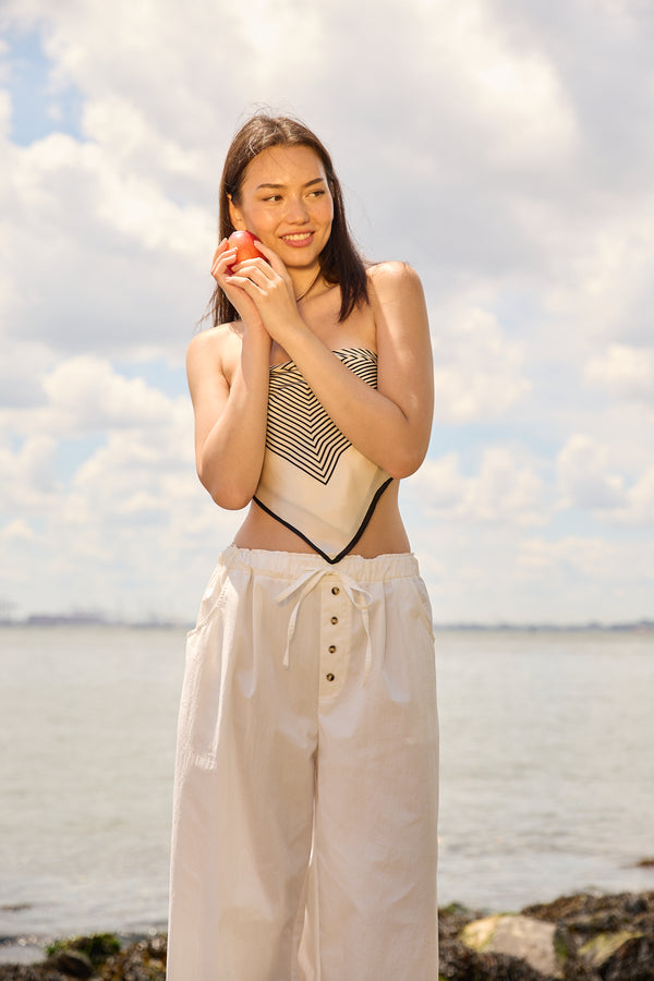 Woman wearing Du & Berry striped scarf top and white wide-leg pants by the water on a sunny day
