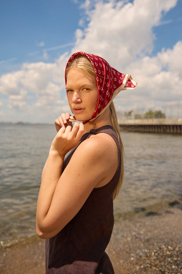 Woman wearing Du & Berry Square Silk Scarf in Red tied around her head by the beach