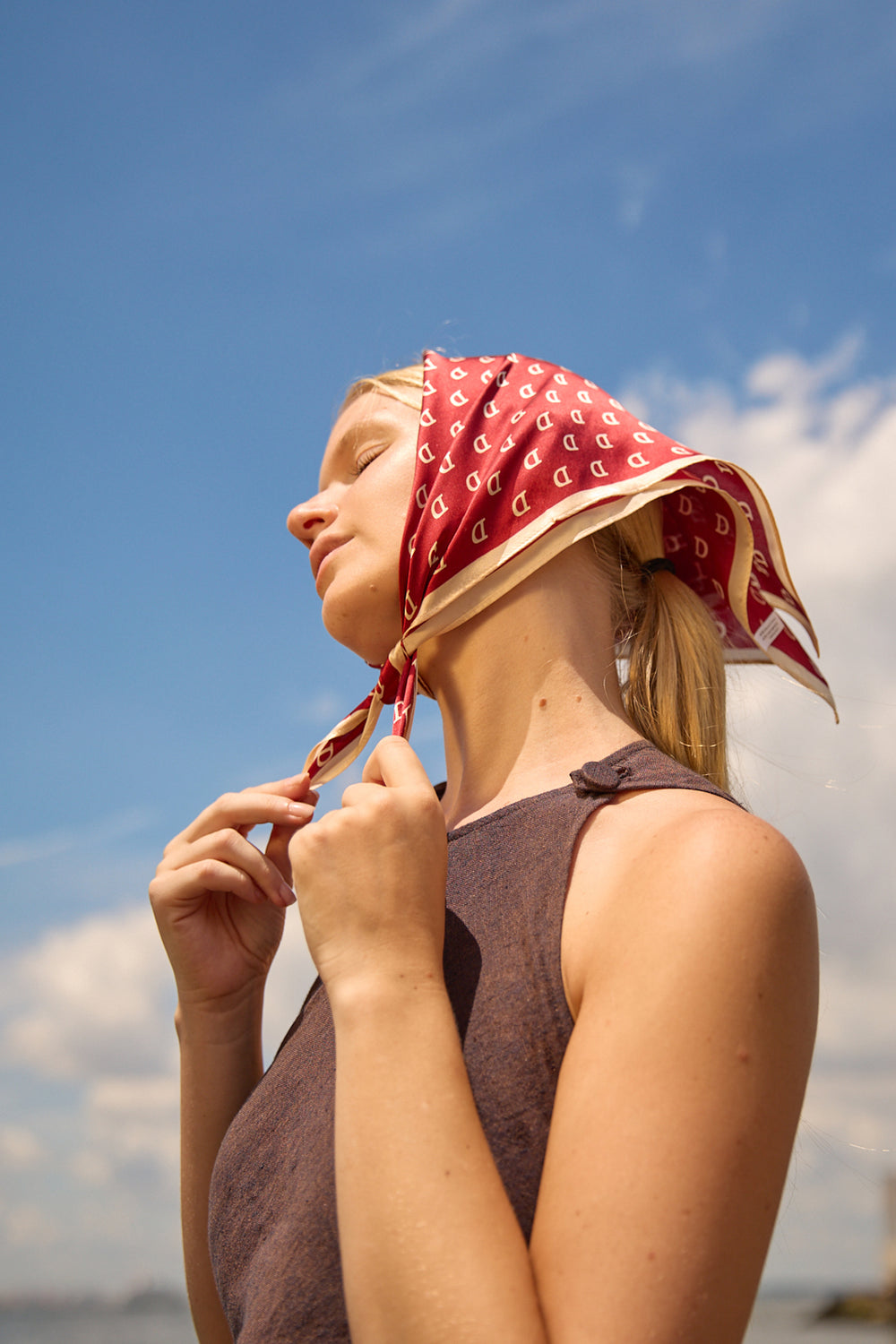 Woman wearing Du & Berry Square Silk Scarf in Red tied around her head by the beach