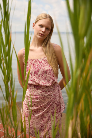 Du & Berry convertible silk wrap dress in pink floral pattern worn by woman outdoors near water
