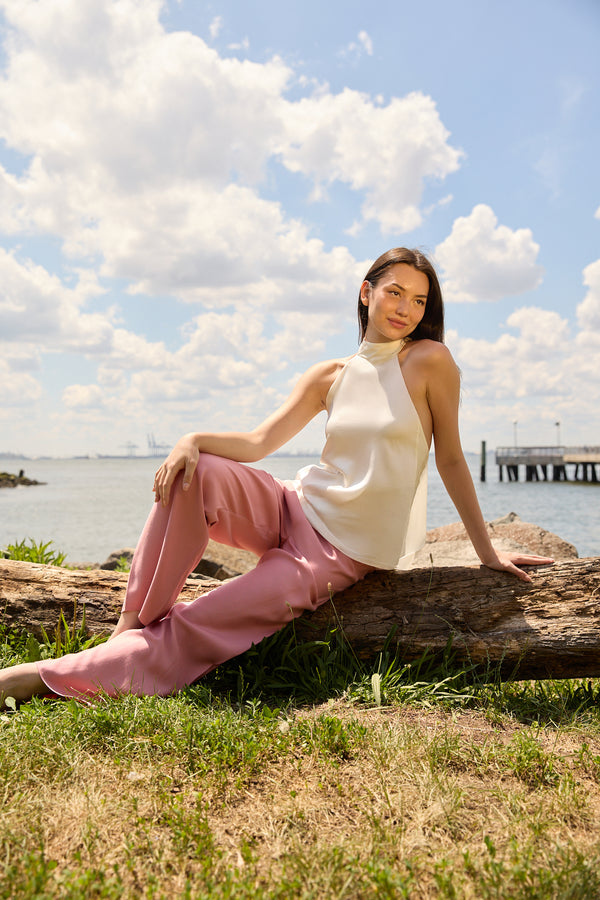 Woman wearing dusty rose straight pants by Du & Berry sitting on a log near the water on a sunny day