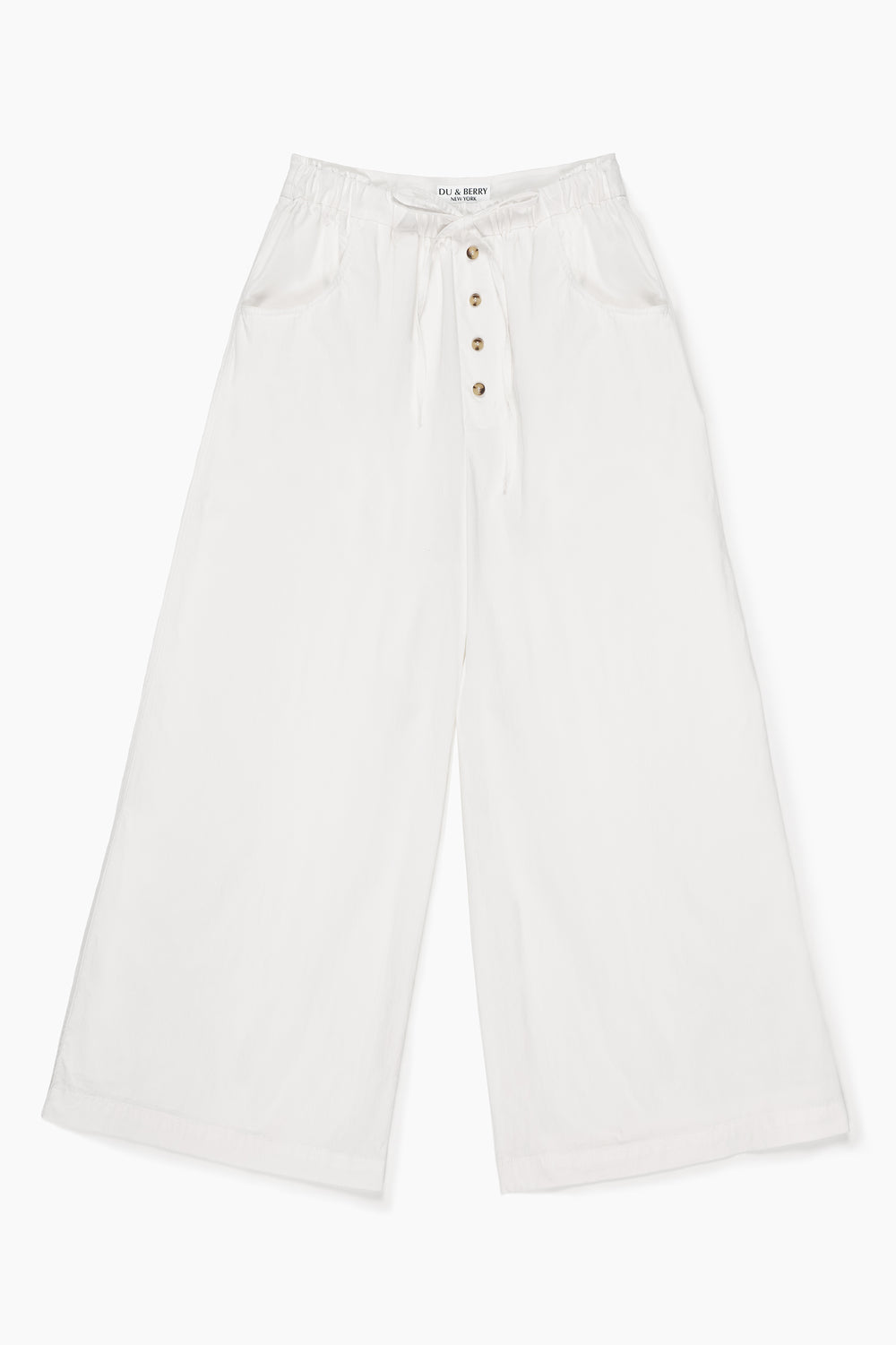 Woman wearing Du & Berry white cotton palazzo pants standing by the rocky lakeside under a blue sky