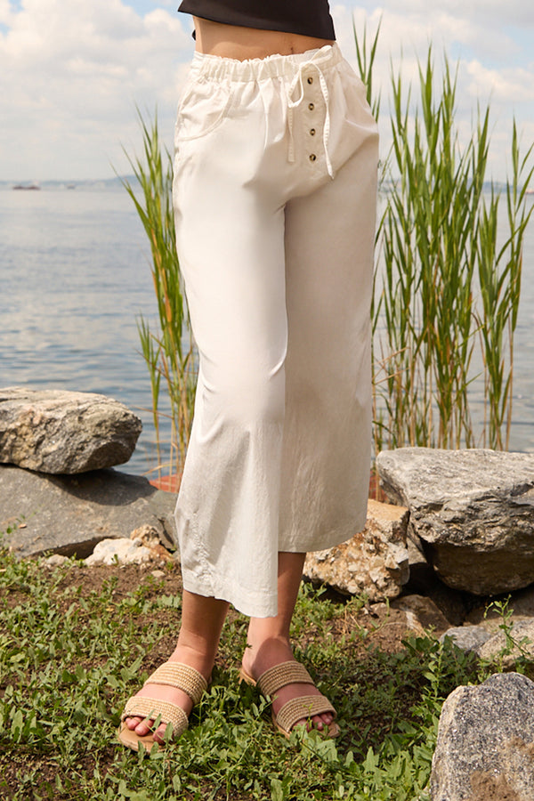 Du & Berry white cotton palazzo pants with button detail worn outdoors near water and rocks